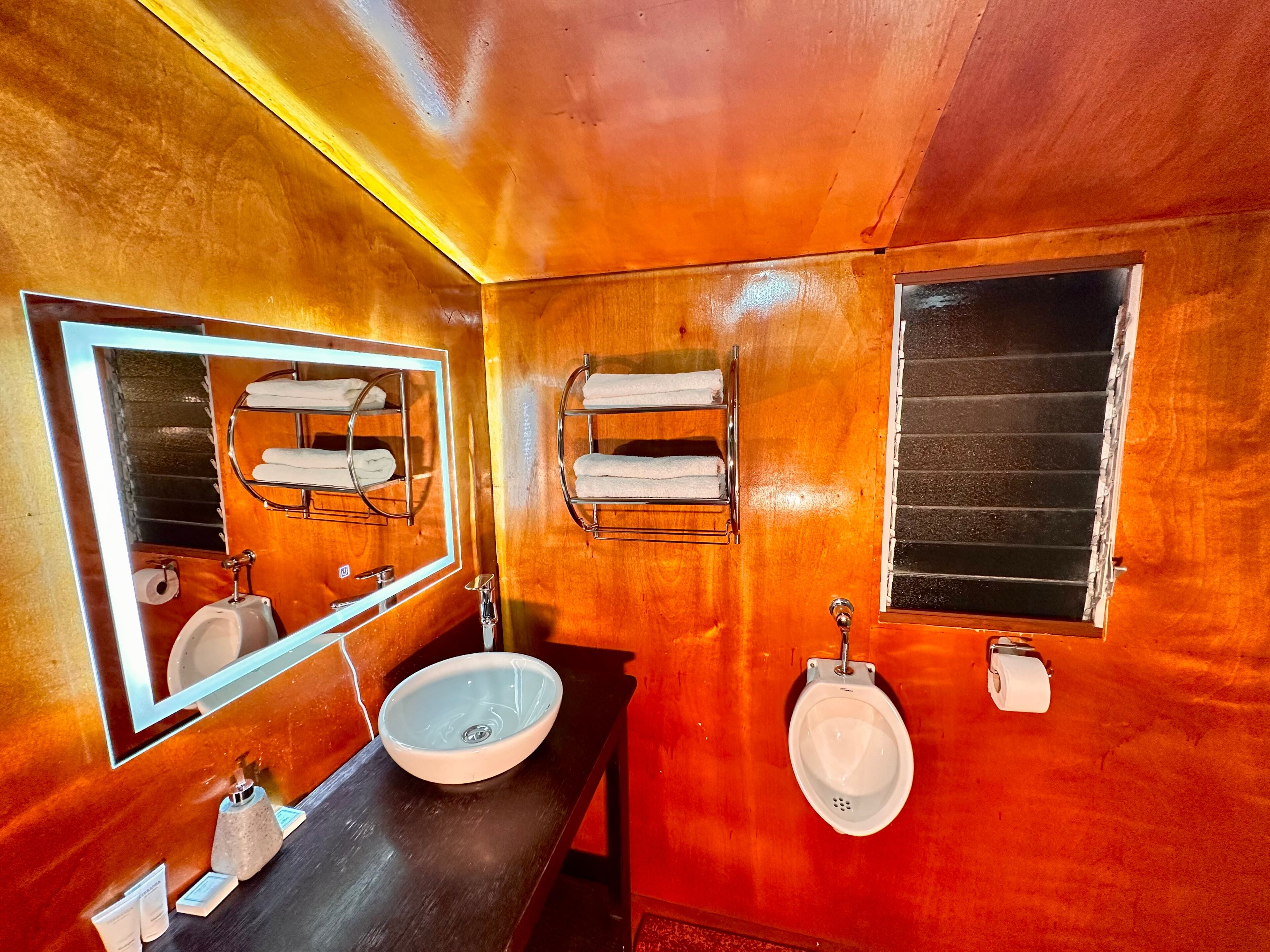 A wooden bathroom with a large mirror, two sinks, and towel racks.