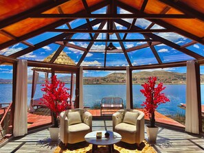 Un espacio de estar al aire libre cubierto con dos sillas y una mesa, con vistas a un lago y colinas.