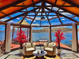 Un espacio de estar al aire libre cubierto con dos sillas y una mesa, con vistas a un lago y colinas.