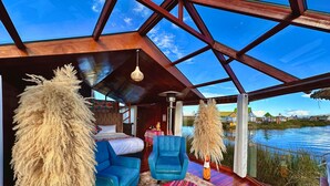 A modern room with a bed, blue armchair, and a view of a body of water through large windows.