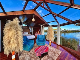 Una habitación moderna con una cama, un sillón azul y vista a un cuerpo de agua a través de amplias ventanas.