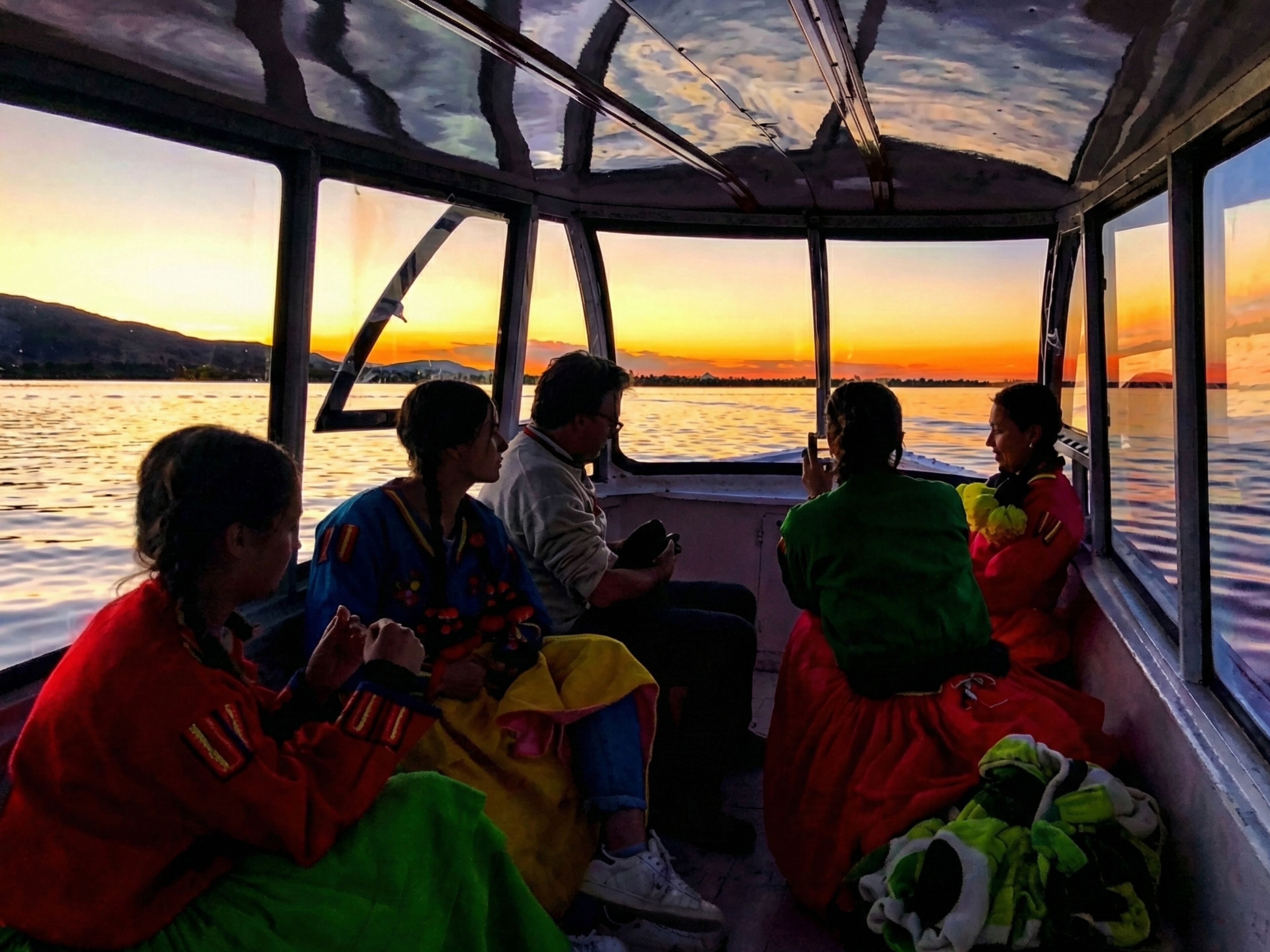 A group of people on a boat during sunset, with a view of the water and distant land.