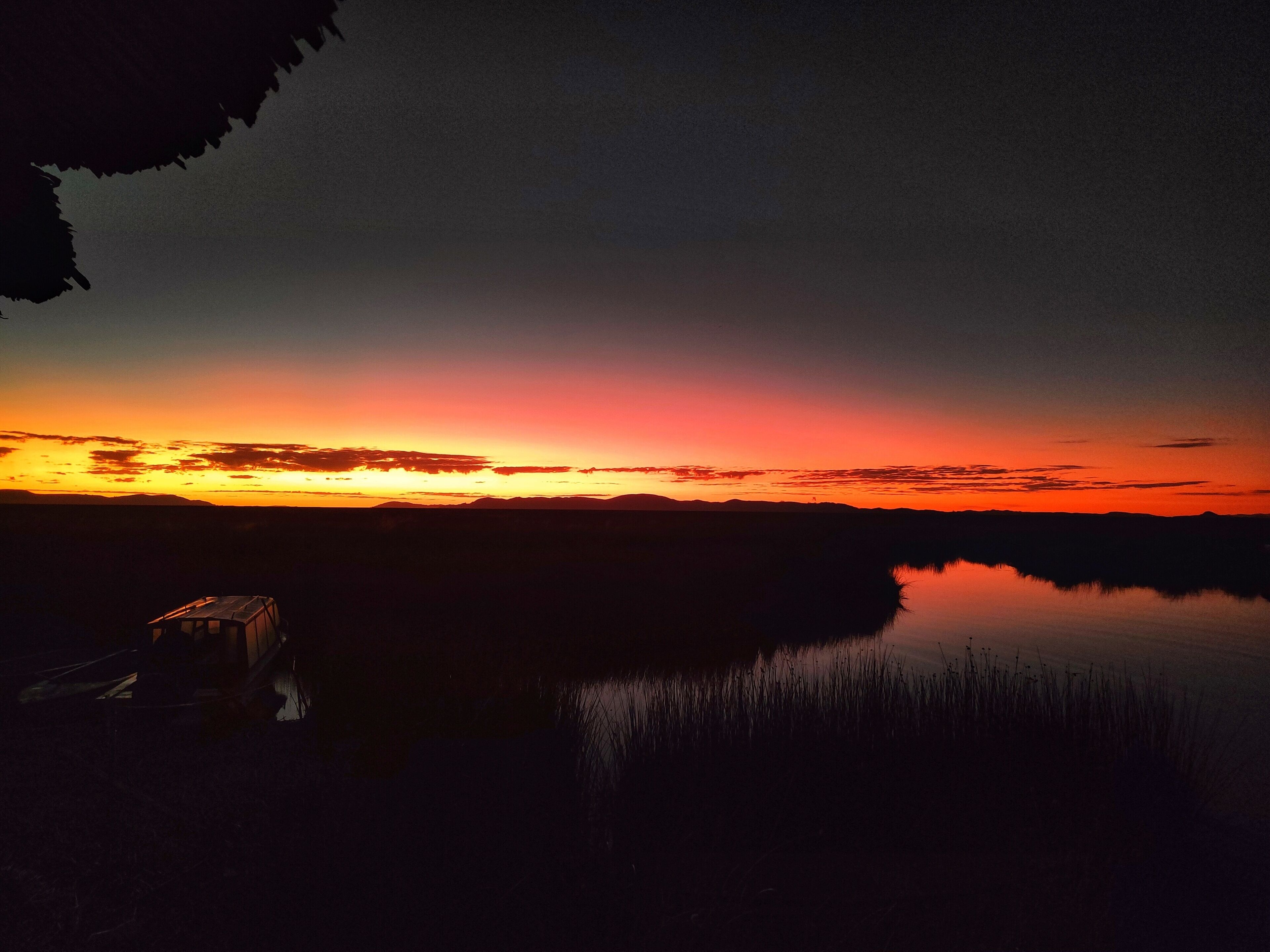 A sunset over a calm body of water with a silhouette of a building on the left.