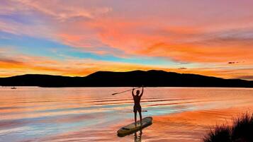 A person paddleboarding on a calm lake during sunset with mountains in the background.