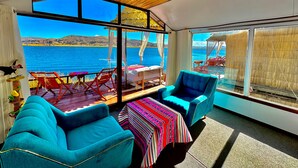 A room with a large window overlooking a body of water, a wooden ceiling, and blue chairs.