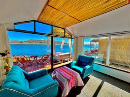 Una habitación con un gran ventanal con vistas a un cuerpo de agua, techo de madera y sillas azules.