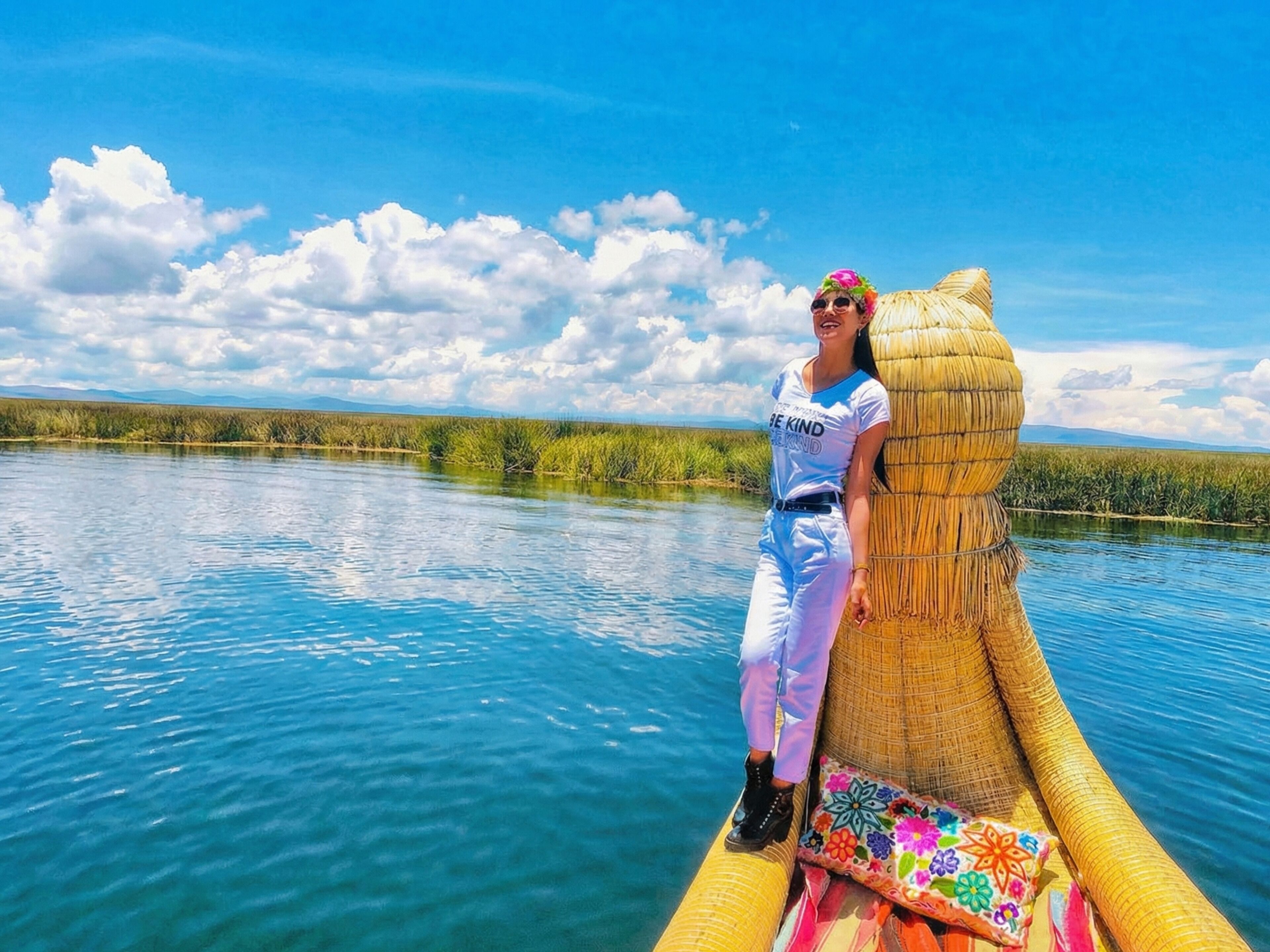 A person sitting on a straw boat in a calm body of water with a clear sky and distant mountains.