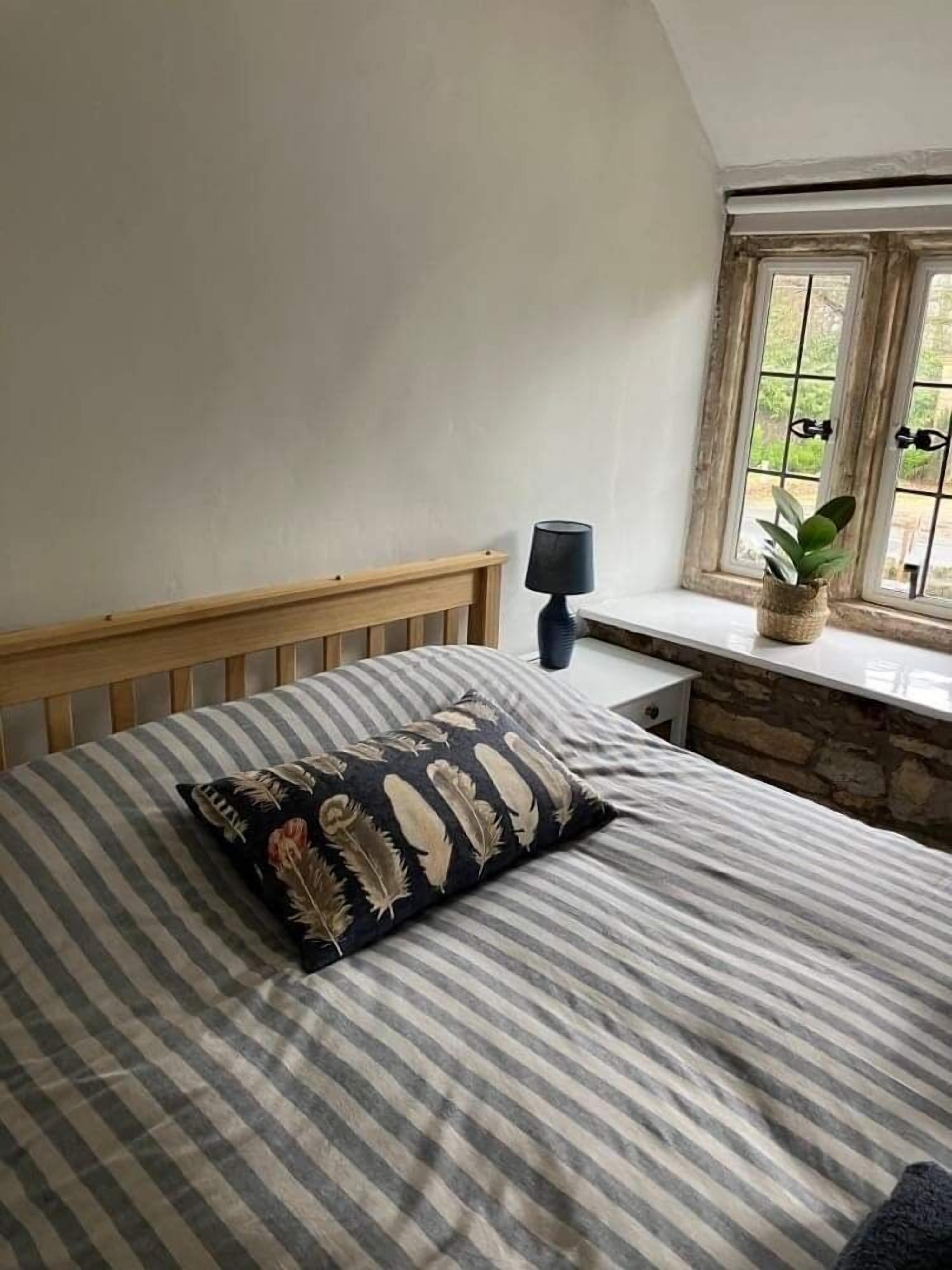 A bedroom with a bed, a nightstand, a lamp, and a window with a view of greenery.