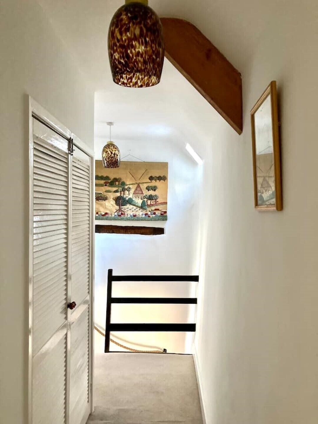 A narrow hallway with a wooden ceiling beam, a hanging lamp, and a painting on the wall.