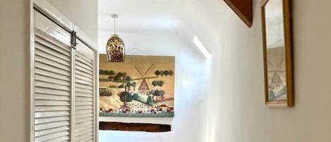 A narrow hallway with a wooden ceiling beam, a hanging lamp, and a painting on the wall.