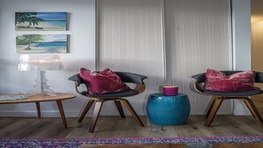 A room with two chairs, a small table, a lamp, and a blue stool. There are two paintings on the wall and a sliding door. - Great Location to the hospitals: 2 bed 1 bath Fully furnished. (Honolulu)