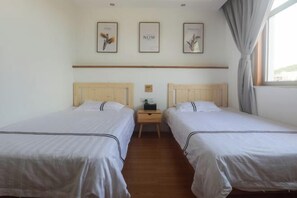 A hotel room with two single beds, a wooden nightstand, and a window with curtains.
