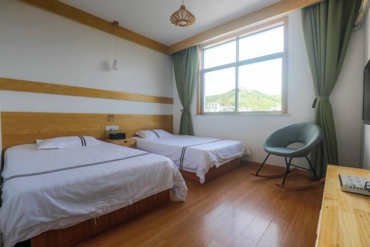 A room with two beds, a wooden floor, a window with curtains, a chair, and a table.