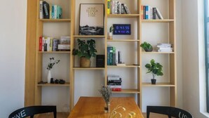 A room with a wooden table, two black chairs, a bookshelf, and a digital clock.