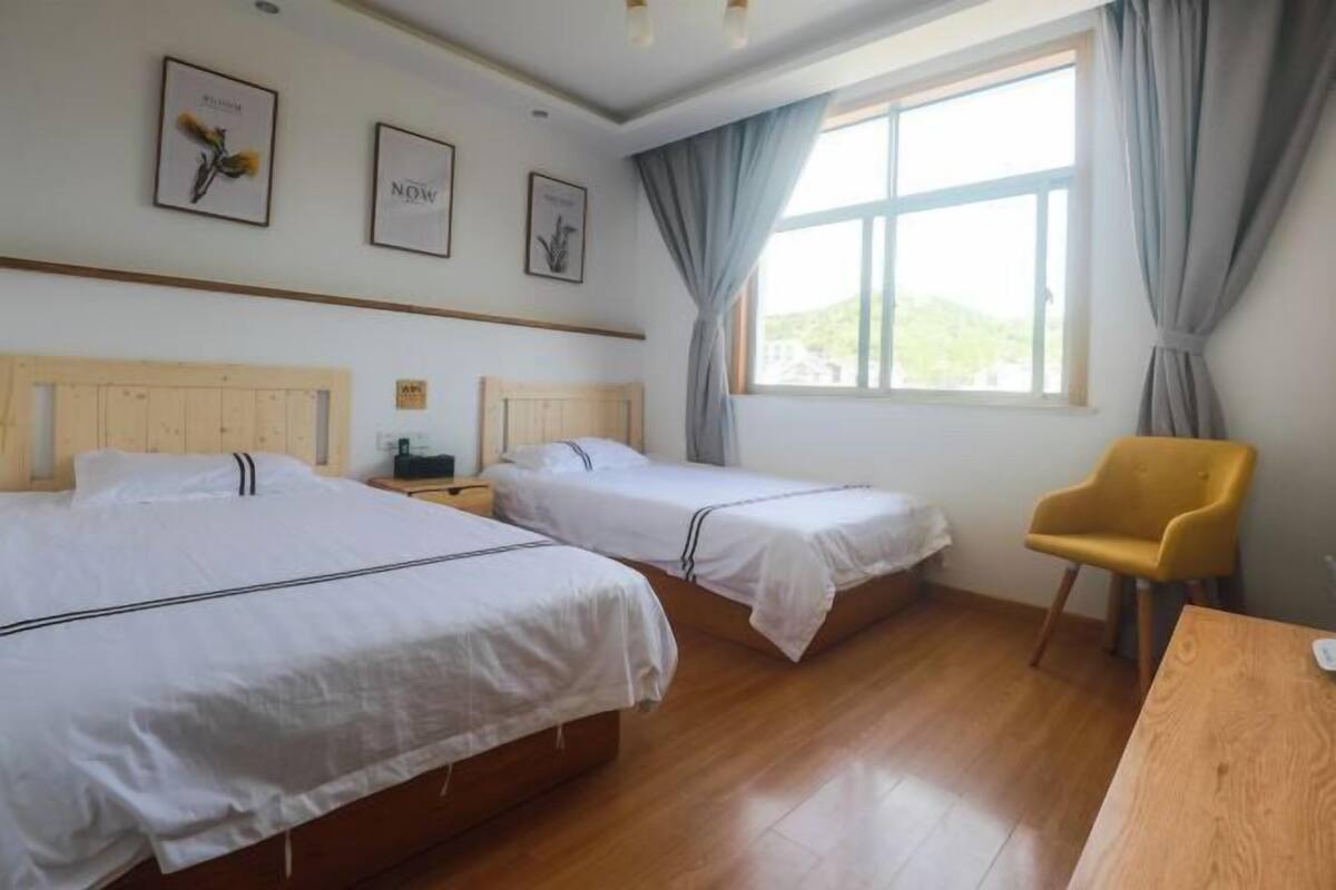 A hotel room with two single beds, a wooden desk, a chair, and a large window with curtains.