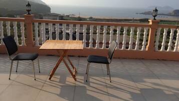 A balcony with a wooden table and two chairs, overlooking a coastal view.