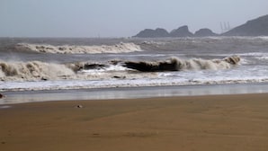 A beach with rough waves and a distant view of a bridge.