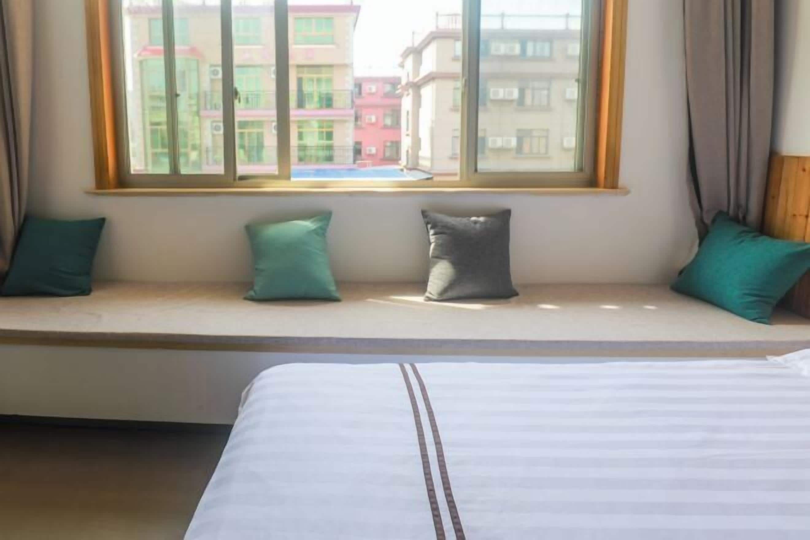 Una habitación de hotel con una cama grande, un asiento junto a la ventana con cojines y vistas a edificios.