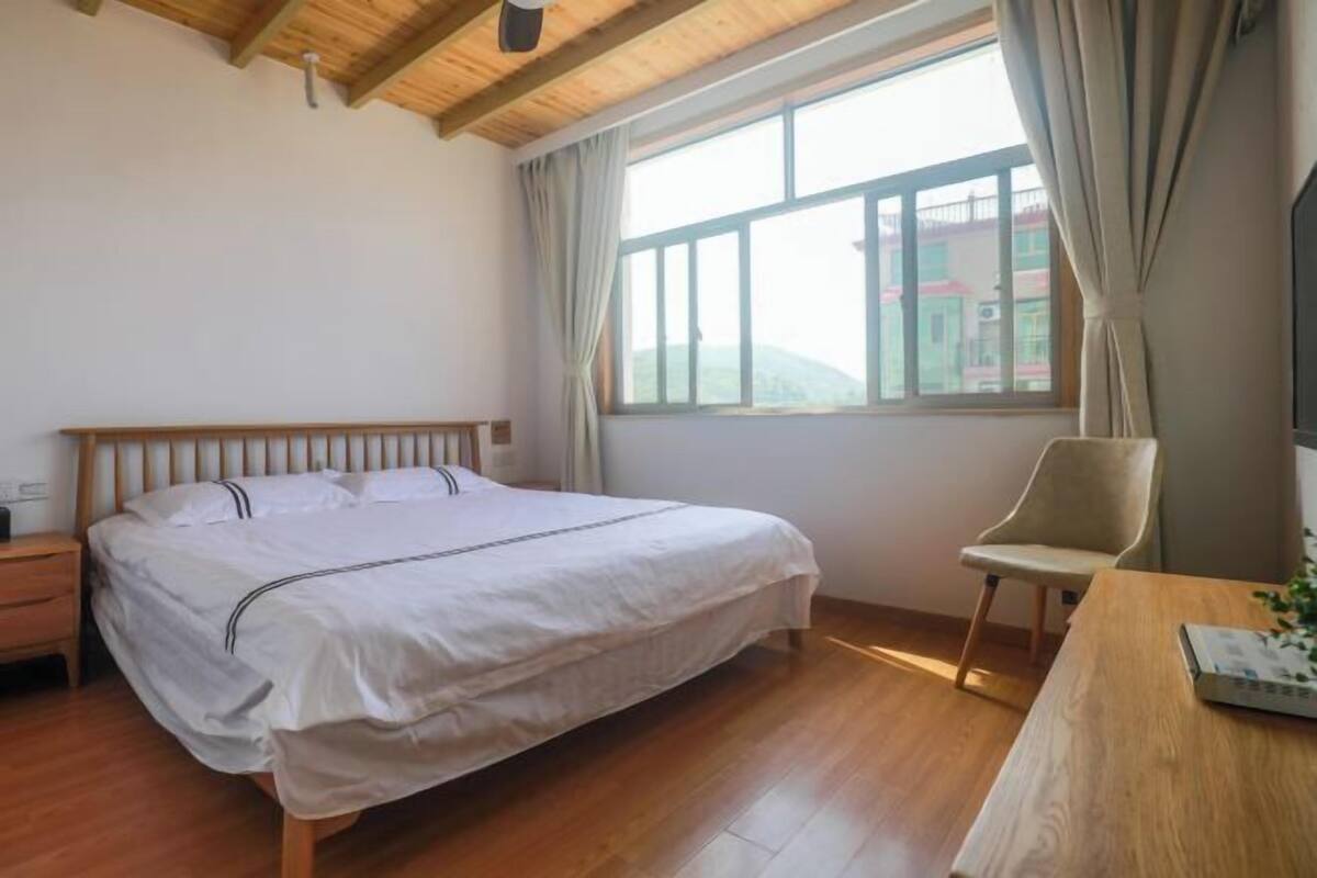 A bedroom with a wooden bed, a nightstand, a chair, a desk, and a window with curtains.