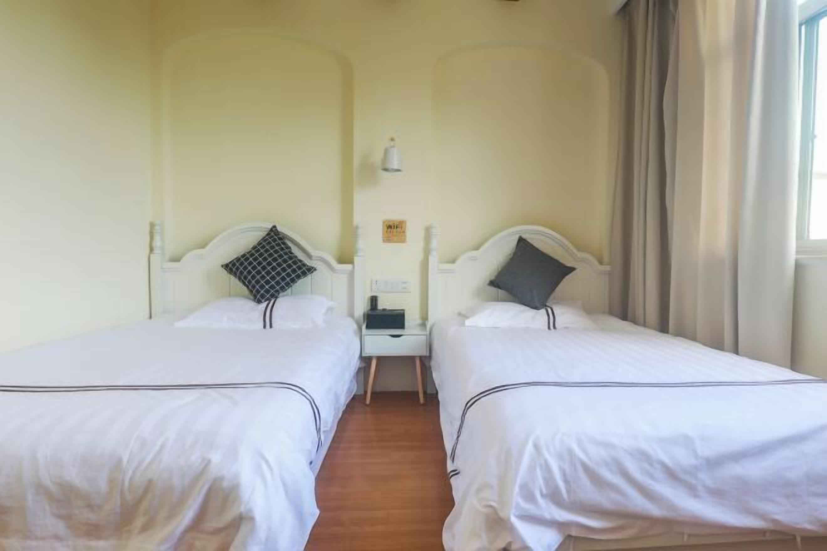 Une chambre avec deux lits simples, une petite table de chevet avec une lampe, un panneau indiquant la disponibilité du Wi-Fi et une fenêtre avec des rideaux.