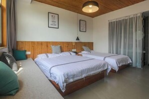 Quarto com duas camas, cabeceira de madeira, um sofá e uma janela com cortinas.