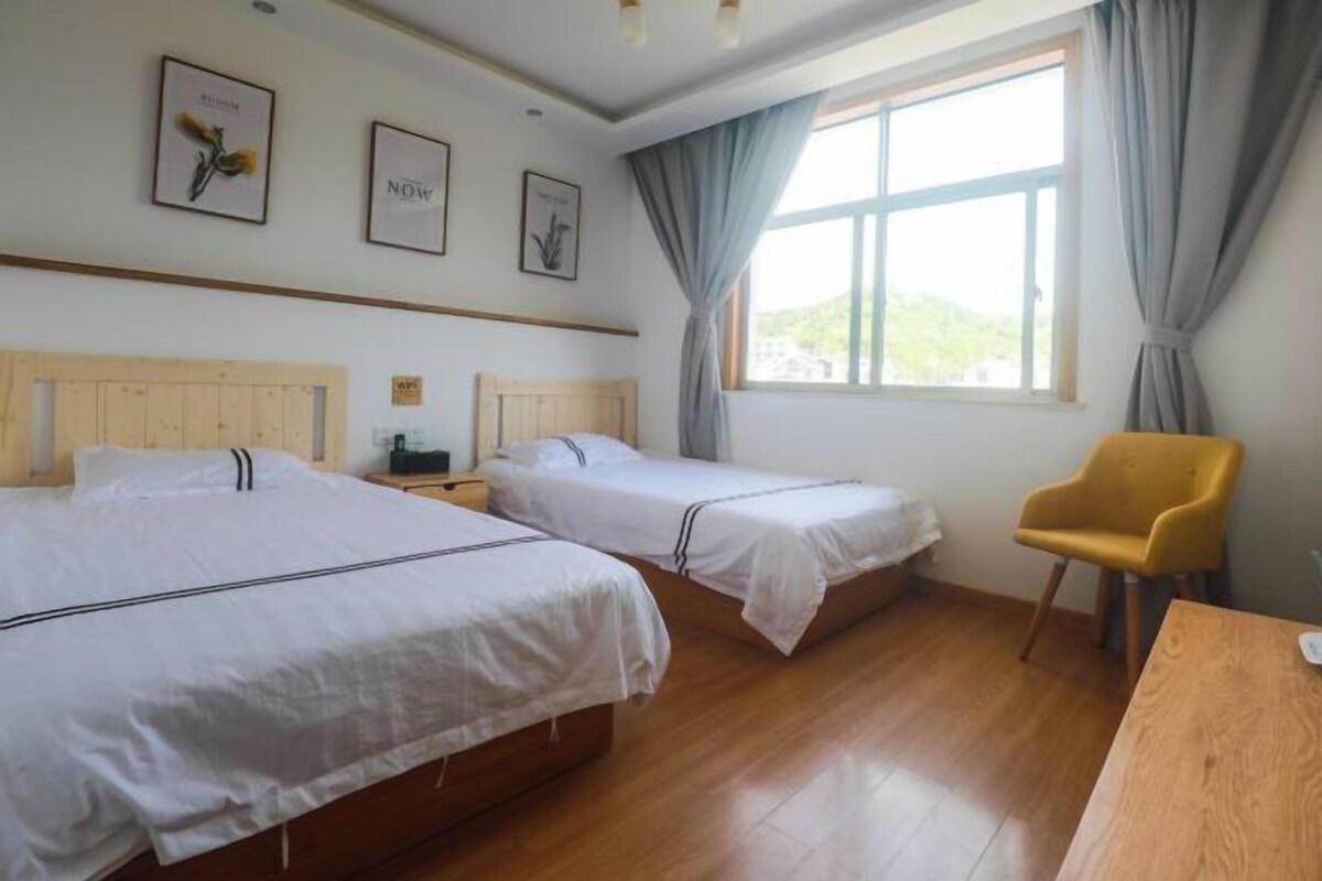 Quarto de hotel com duas camas, uma escrivaninha de madeira, uma cadeira e uma janela com cortinas.