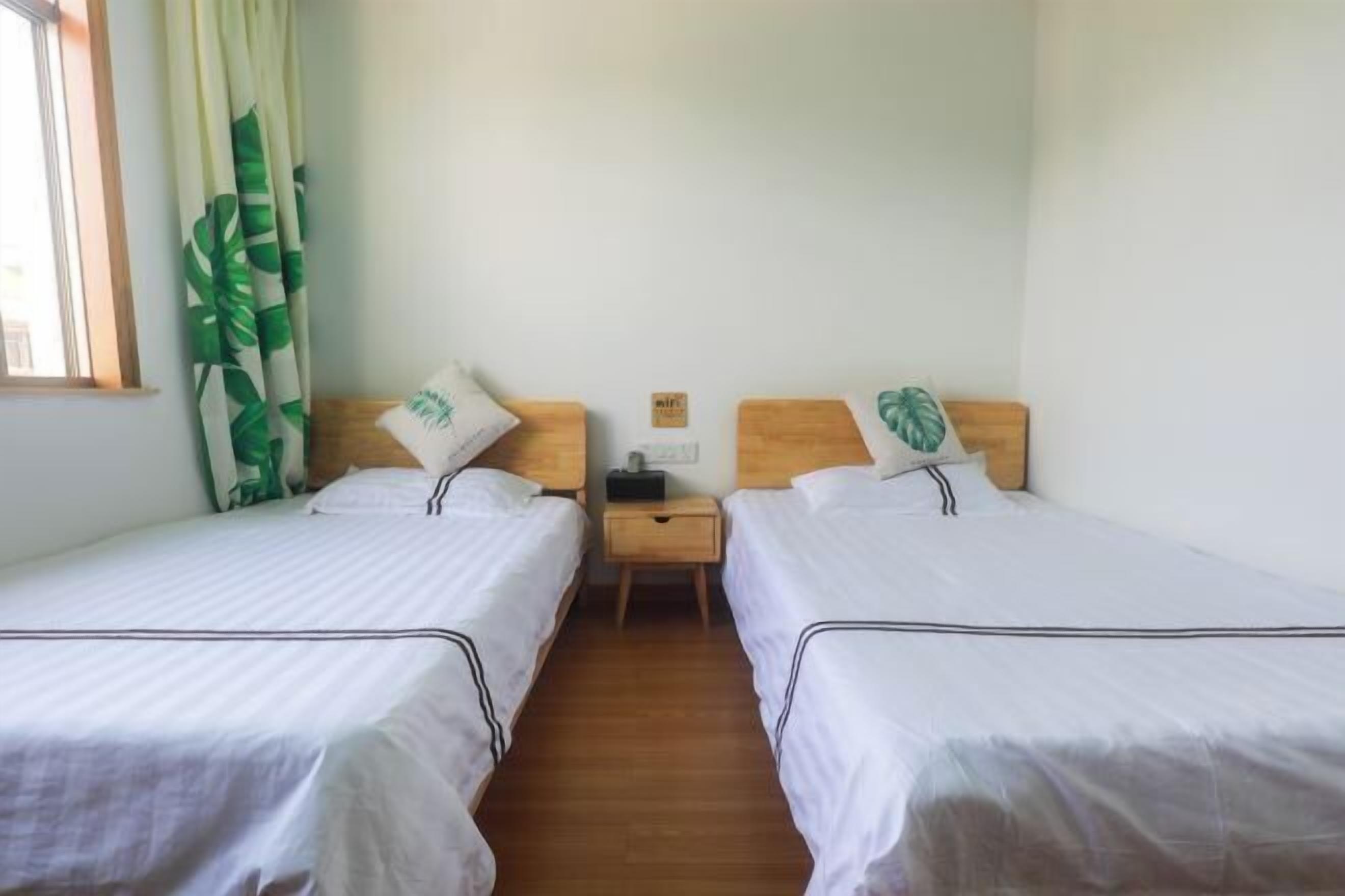 A room with two single beds, wooden nightstands, a small table, and a window with curtains.