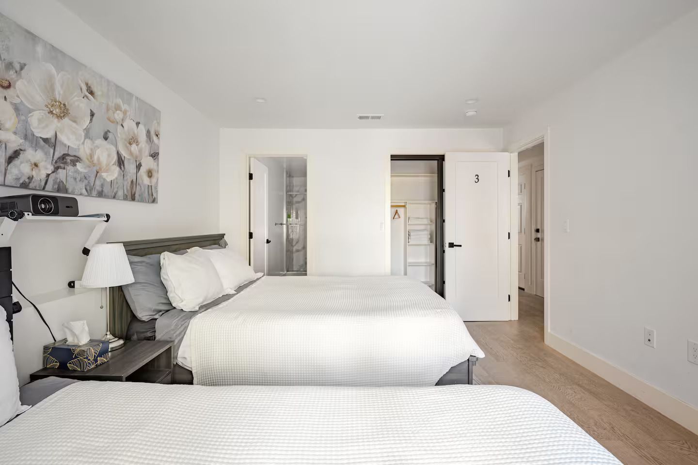 A hotel room with two beds, a nightstand, a lamp, and a painting on the wall.