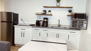 Une cuisine moderne avec des meubles blancs, un réfrigérateur en acier inoxydable, une machine à café, un four à micro-ondes et une table à manger avec quatre chaises blanches.