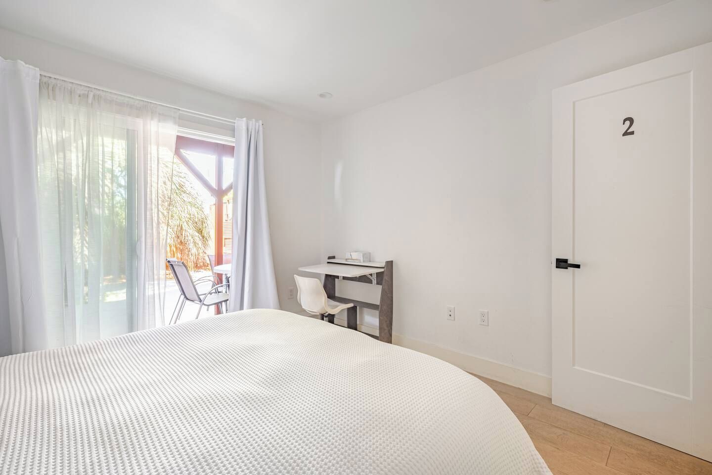 A hotel room with a large bed, a desk, and a chair. There is a door with the number 2 on it.