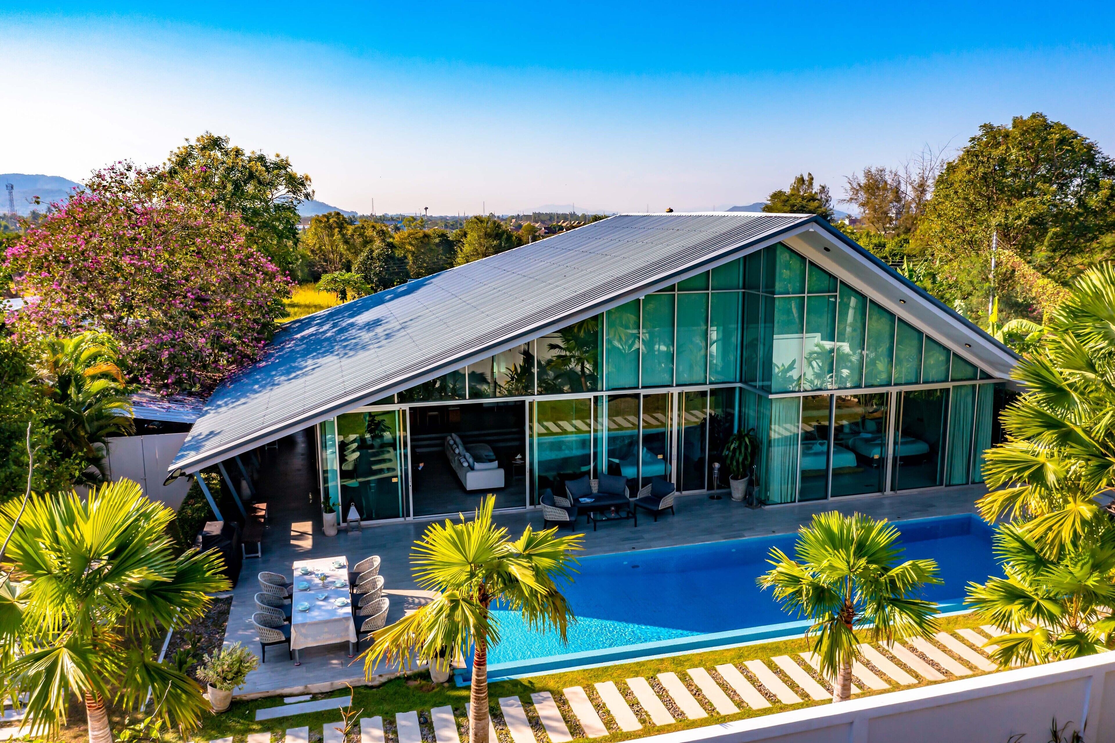 A modern house with a large glass facade, a swimming pool, and a patio area with outdoor furniture.