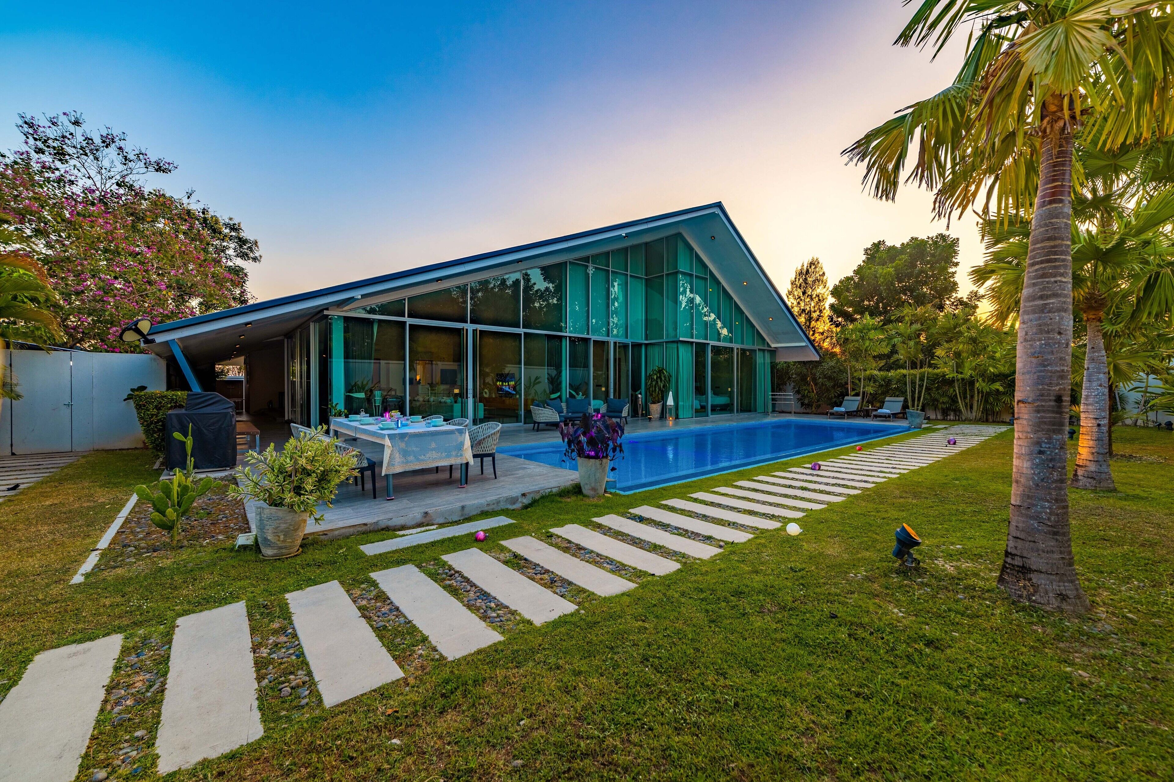 A modern house with a large glass facade, a swimming pool, and a well-maintained garden.