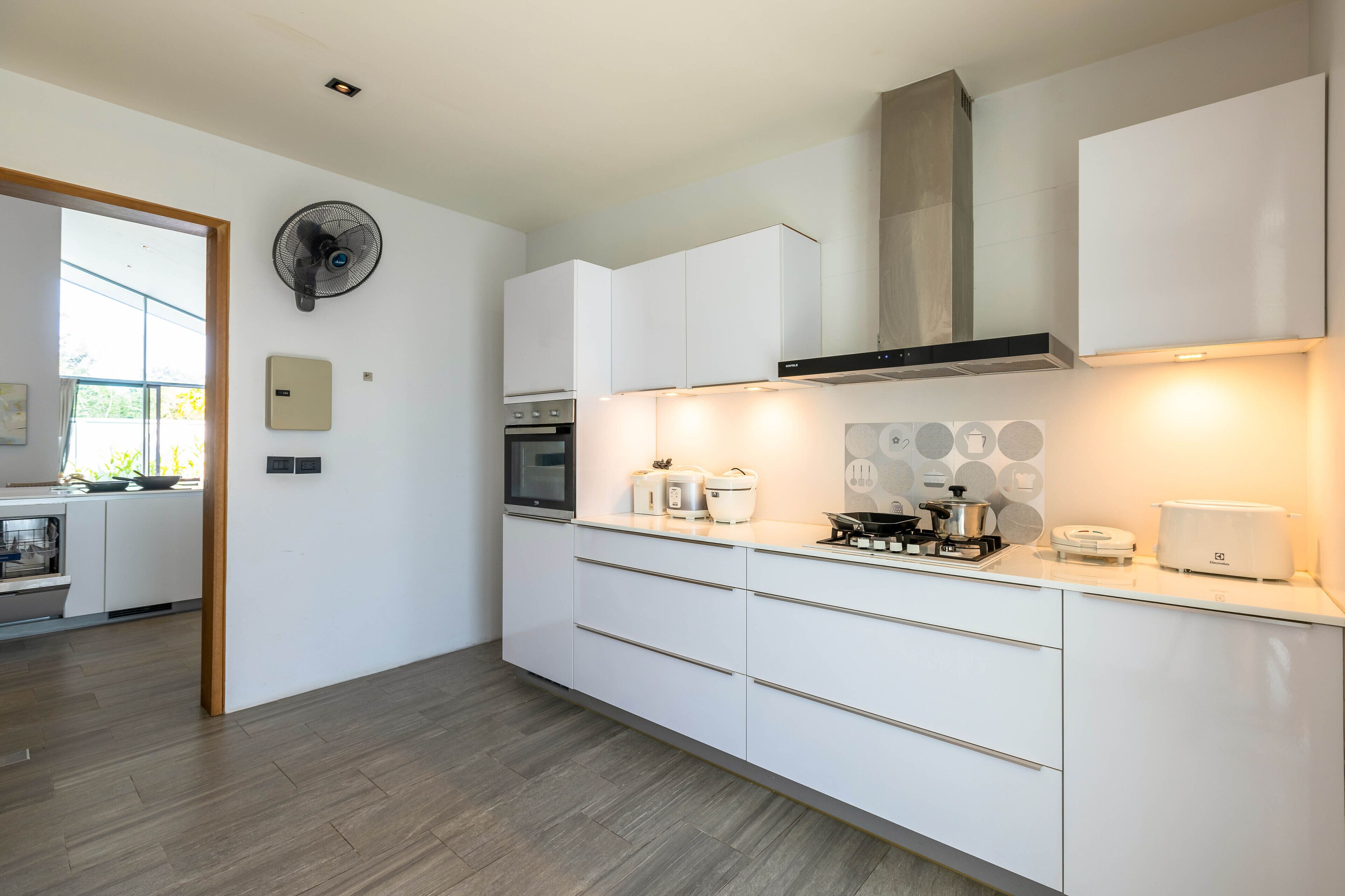 A modern kitchen with white cabinets, a built-in oven, a stove, and a fan.