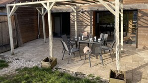 Ein Holzhaus mit einer überdachten Terrasse, die einen Tisch, Stühle, eine Pergola und einen Blick ins Innere bietet.