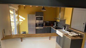 Kompakti keittiö, jossa on keskeinen saareke, integroidut kodinkoneet ja keltainen tehosteseinä.