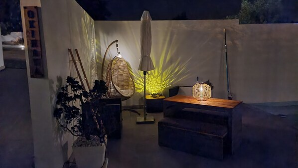 Een terras met een rieten stoel, een tafel met een lamp en een potplant.