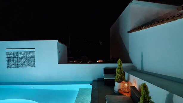 Un espai exterior modern amb piscina, zona de seients i vistes a la ciutat de nit.