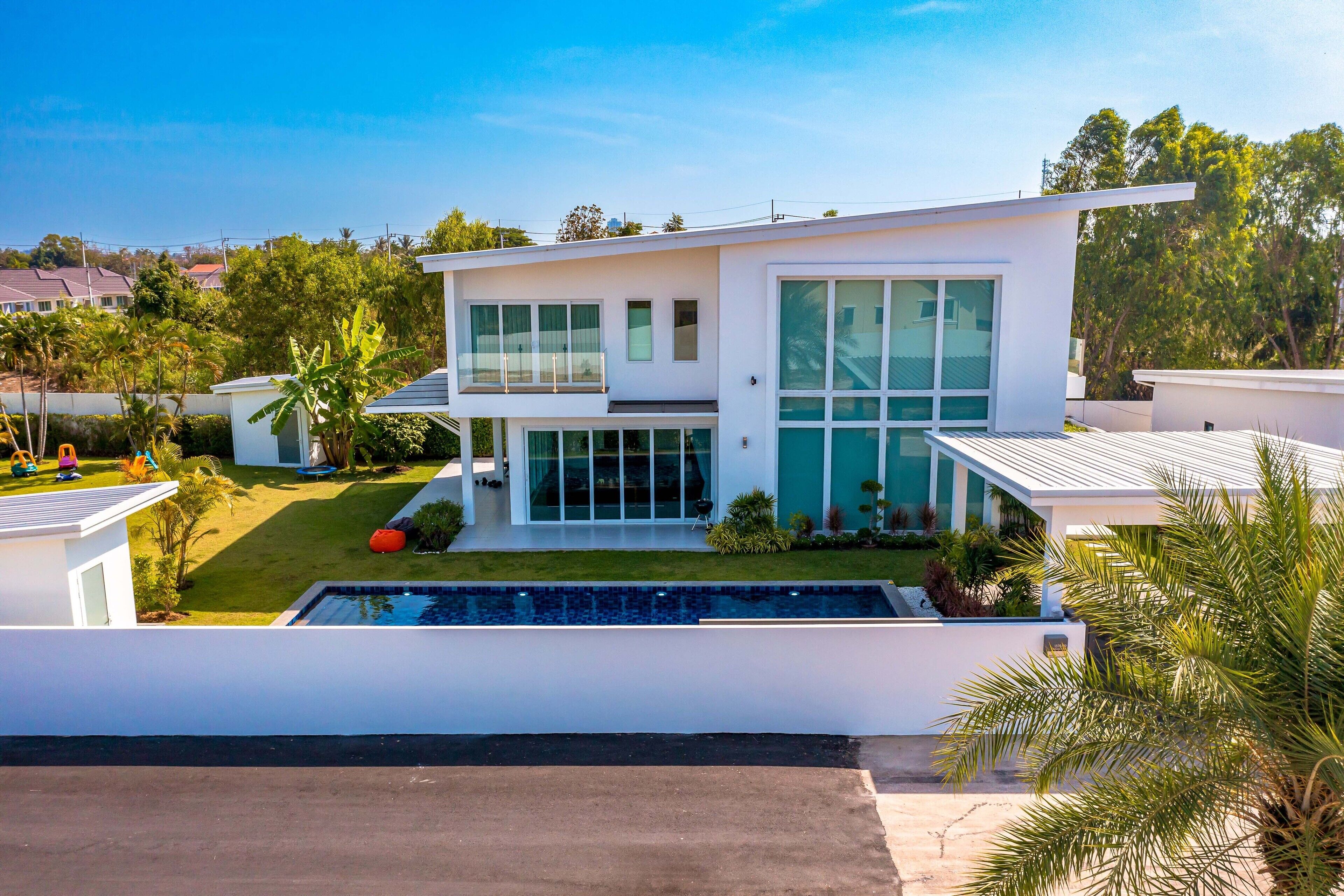 Ein modernes, zweistöckiges Haus mit großem Panoramafenster, Schwimmbad und gepflegtem Rasen.