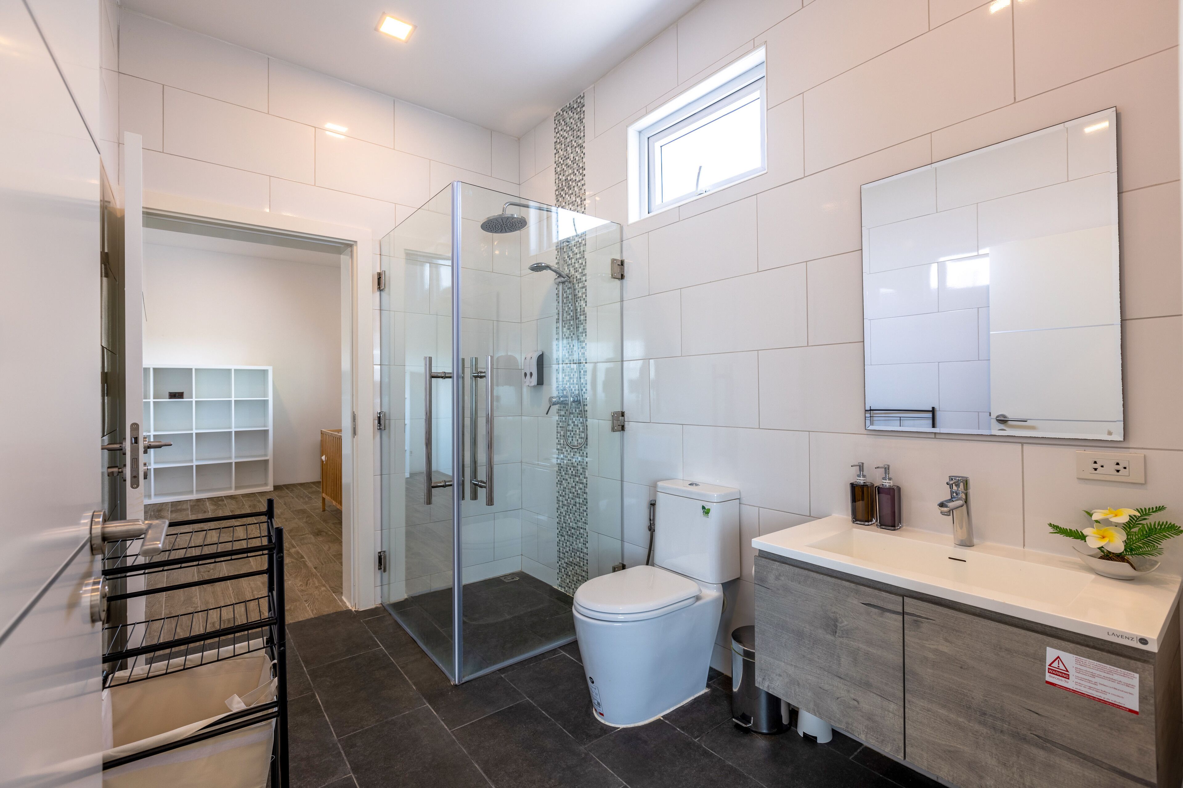 Une salle de bain moderne avec une douche à parois de verre, des toilettes, un meuble-lavabo avec un miroir et une petite fenêtre.