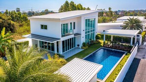 Ett modernt hus i två våningar med ett stort glasfönster, en swimmingpool och en välskött gräsmatta.