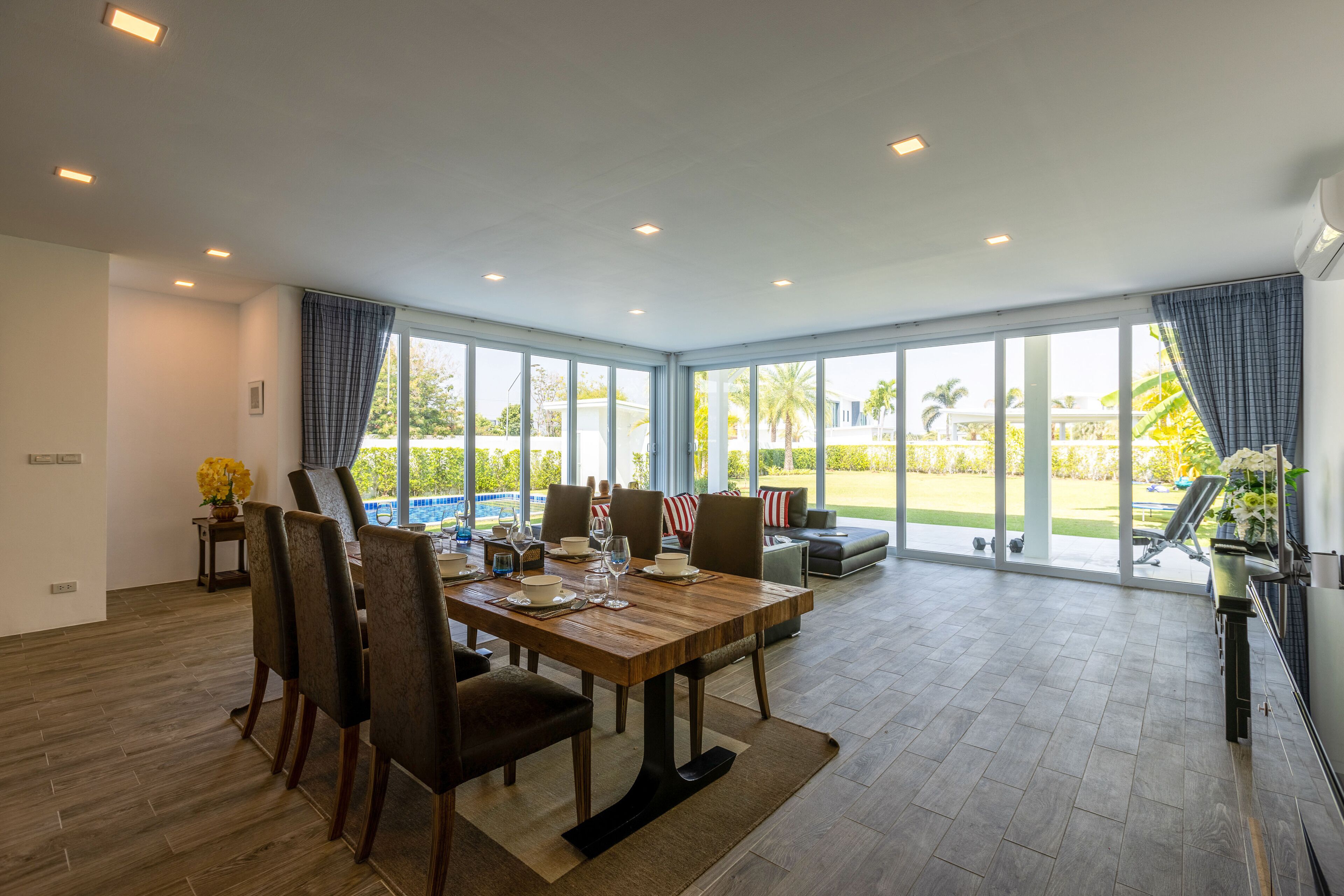Un comedor espacioso con una mesa y sillas de madera, ventanas amplias con vistas al exterior y una cocina moderna visible a la derecha.