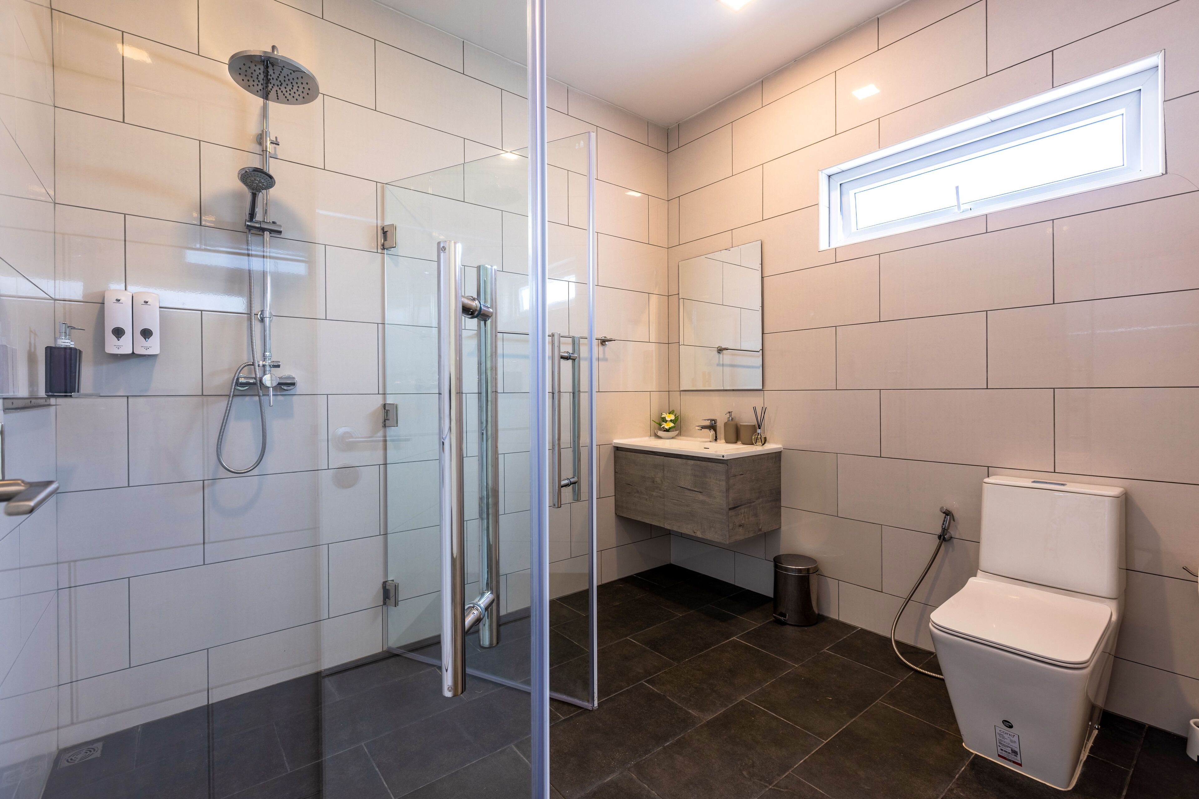 Ein modernes Badezimmer mit einer Duschkabine, einer weißen Toilette und einem Waschtisch mit Spiegel.