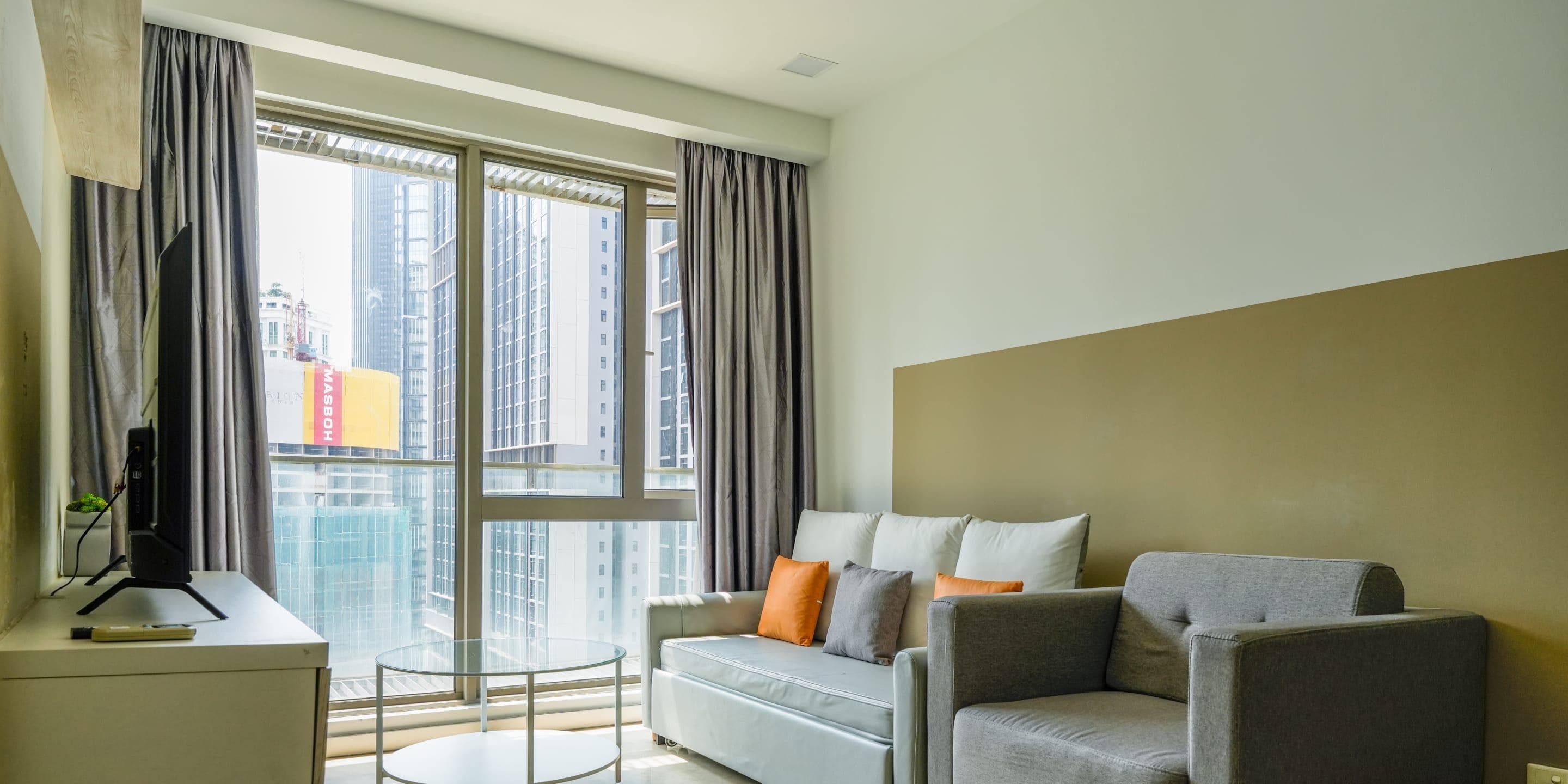 A modern living room with a grey sofa, a small round table, and a large window with curtains.