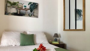 A neatly made bed with a green and white color scheme, a bedside table with a lamp and books, and a wall-mounted mirror. - Bungalow, 10-minute walk from Etang-Salé les Bains beach, sleeps 2 to 4. (L'Étang-Salé)
