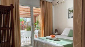 A hotel room with a bed, a table with chairs, a lamp, and a view of the outdoors. - Bungalow, 10-minute walk from Etang-Salé les Bains beach, sleeps 2 to 4. (L'Étang-Salé)