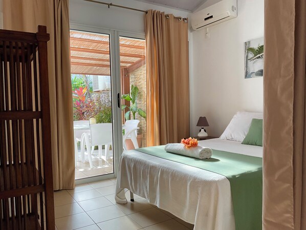 A hotel room with a bed, a table with chairs, a lamp, and a view of the outdoors.