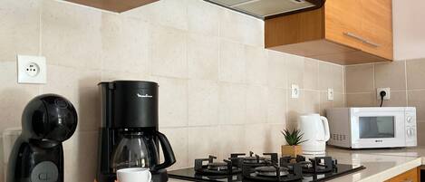 Una cocina moderna con cafetera, hervidor, microondas y estufa a gas.