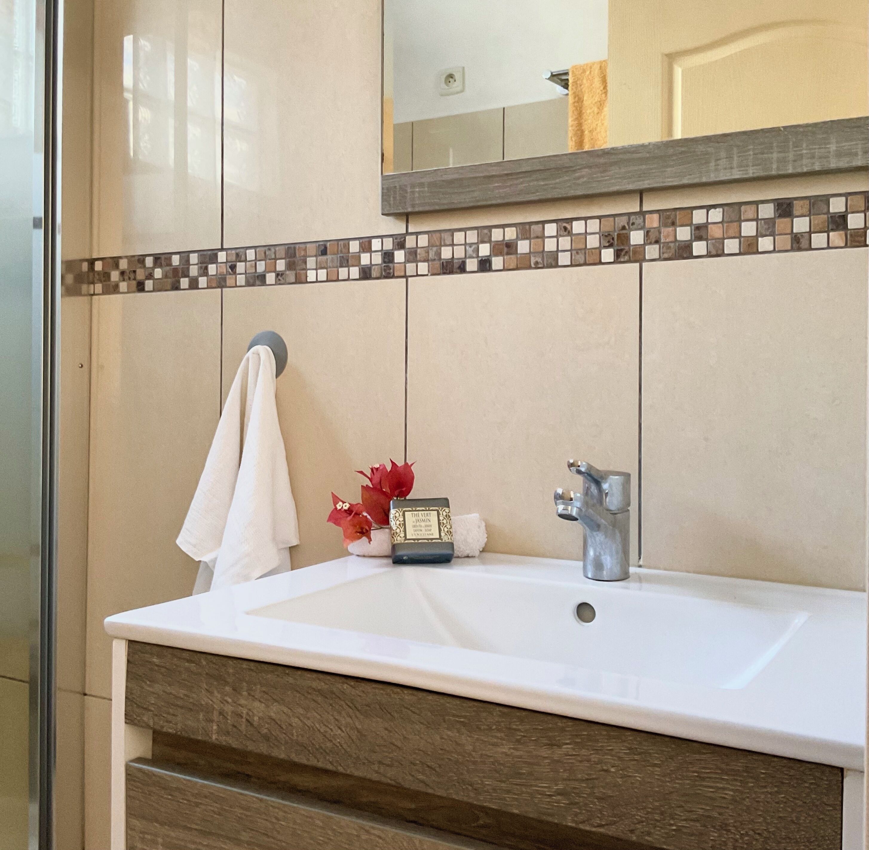 Un bagno con un lavandino bianco, uno specchio sopra e uno schienale piastrellato.