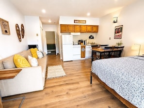 A compact living space with a kitchenette, a sofa with cushions, a bed, and a dining area.