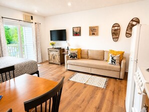 En hyggelig stue med sofa, spisebord, fjernsyn og et køkken.